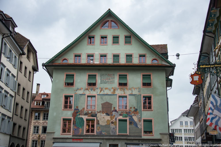 Green-gabled Lucerne house with pink-trimmed windows and narrative murals painted across the façade.