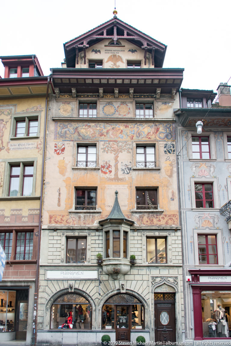 Historic Lucerne façade with arcades, heraldic paintings, decorative murals, and deep projecting eaves.
