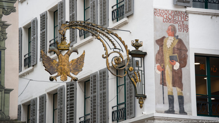 Gilded double-headed-eagle hotel sign beside a wall painting stating that Goethe lodged here in 1779.