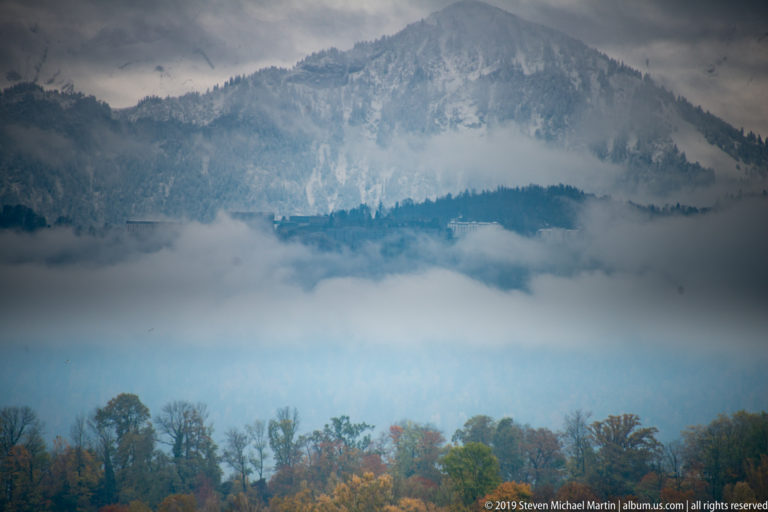 Forested mountain rising through bands of mist above an autumn-colored Lake Lucerne shoreline.