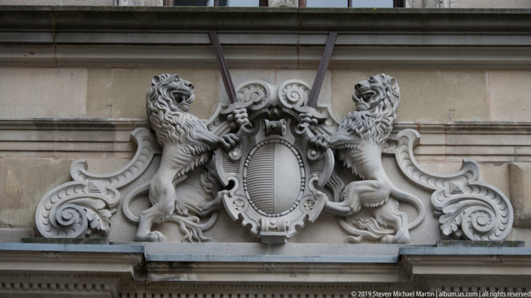 Carved stone relief of two rampant lions flanking an oval shield amid large scrolling ornament.