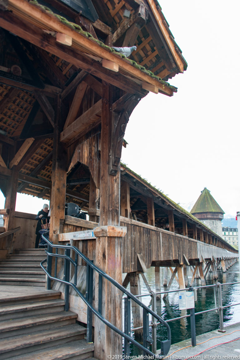 Close side view of Kapellbrücke timber posts, braces, roof trusses, and pile supports above the Reuss River.