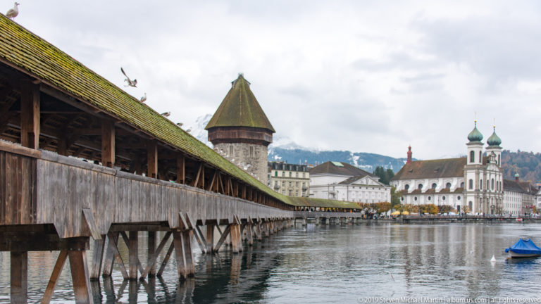 Kapellbrücke beside the Wasserturm with the twin green towers of Lucerne Jesuit Church across the Reuss.