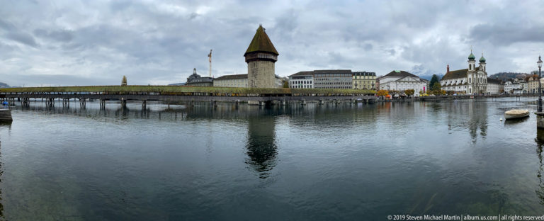 Kapellbrücke crossing the Reuss beside the octagonal Wasserturm, with historic riverfront buildings and the Jesuit Church beyond.