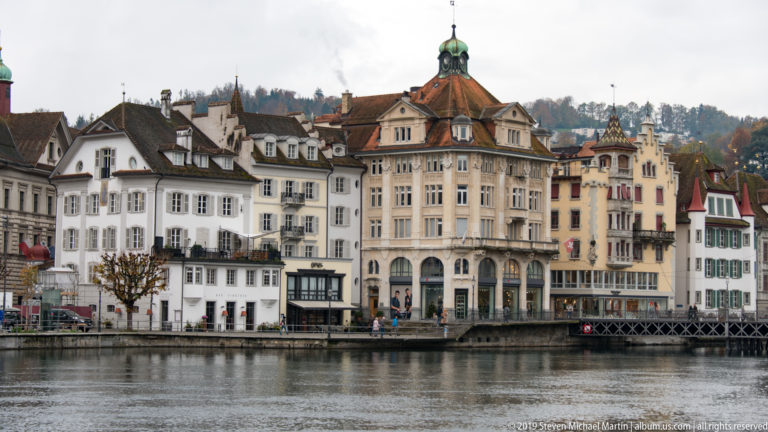 Historic multistory buildings with steep roofs and ornate façades lining the Reuss River in central Lucerne.
