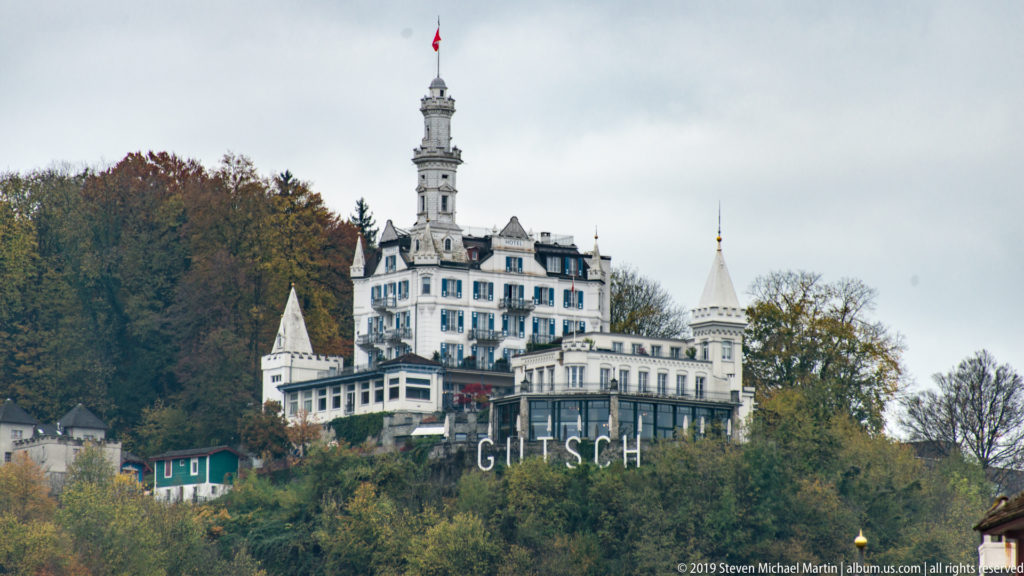 Château Gütsch on a wooded hillside above Lucerne, with its tall central tower and large GÜTSCH letters below.