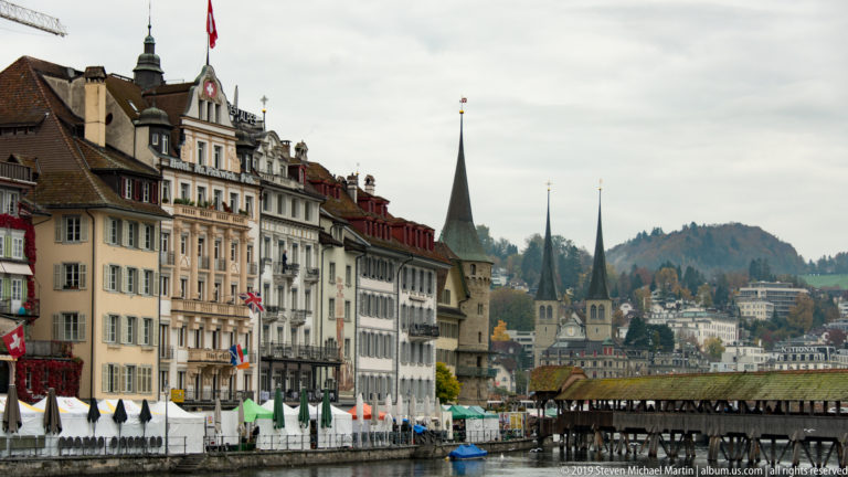 Historic Lucerne waterfront with Jesuit Church towers in the distance and the covered Chapel Bridge entering at right.