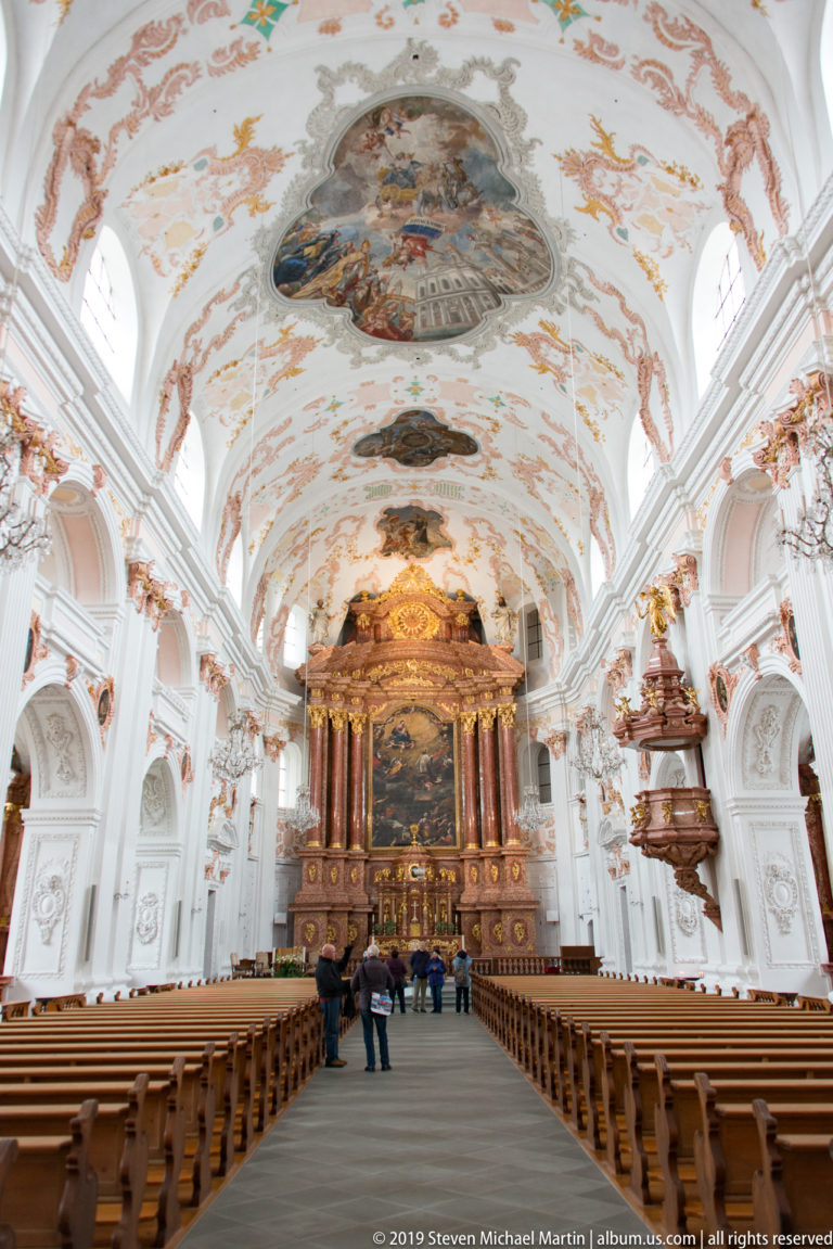 Wide view down the Jesuit Church nave toward the high altar beneath a sequence of ornate ceiling frescoes.