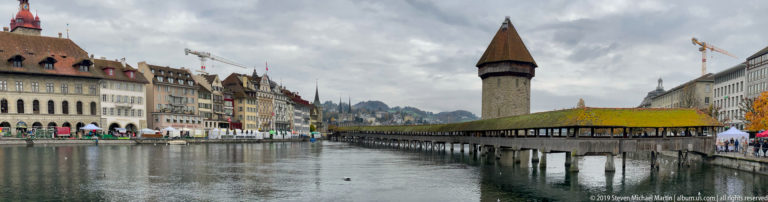 Covered Kapellbrücke and Wasserturm beside the Reuss, with historic multistory façades lining the opposite bank.