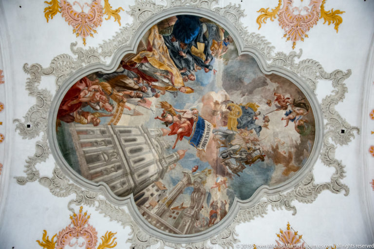 Close view of a lobed Baroque ceiling fresco with clustered figures, clouds, and illusionistic architecture in the Jesuit Church.