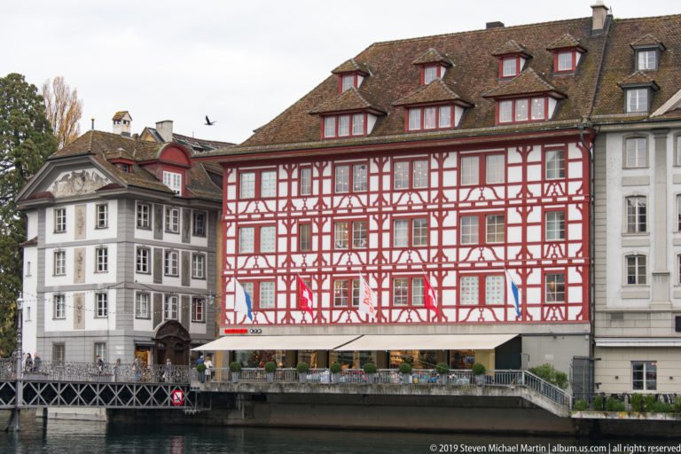 Red-and-white half-timbered multistory building with dormer roof beside the Reuss River in Lucerne.