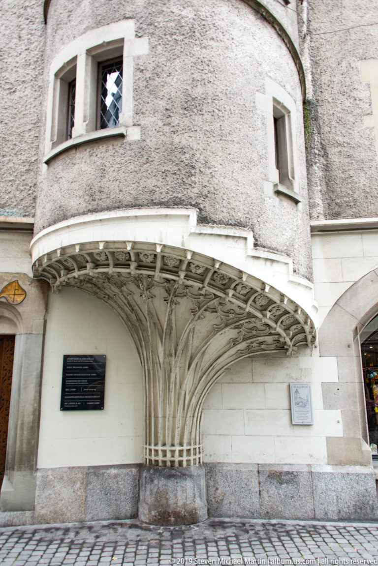 Branching carved stone supports beneath a projecting rounded bay on a historic Lucerne building.