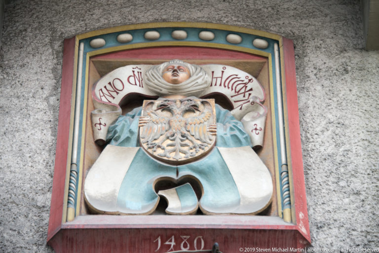 Painted heraldic relief with a double-headed eagle, human head above, and the date 1480 below.