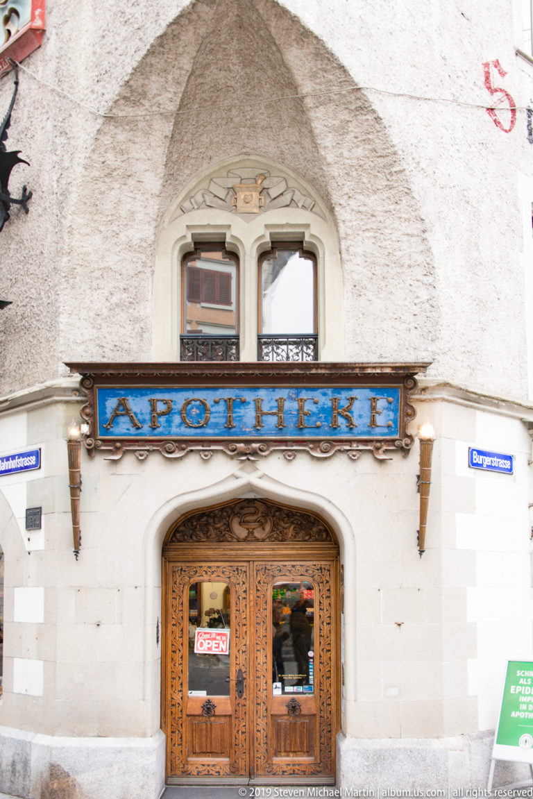 Carved wooden pharmacy entrance beneath a blue-and-gold Apotheke sign on a historic Lucerne façade.