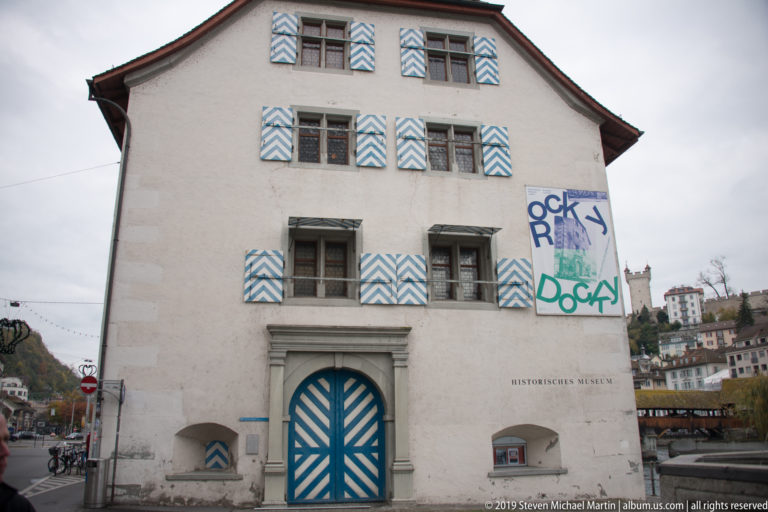 Historisches Museum Lucerne façade with blue-and-white striped shutters, matching doors, and graffiti.