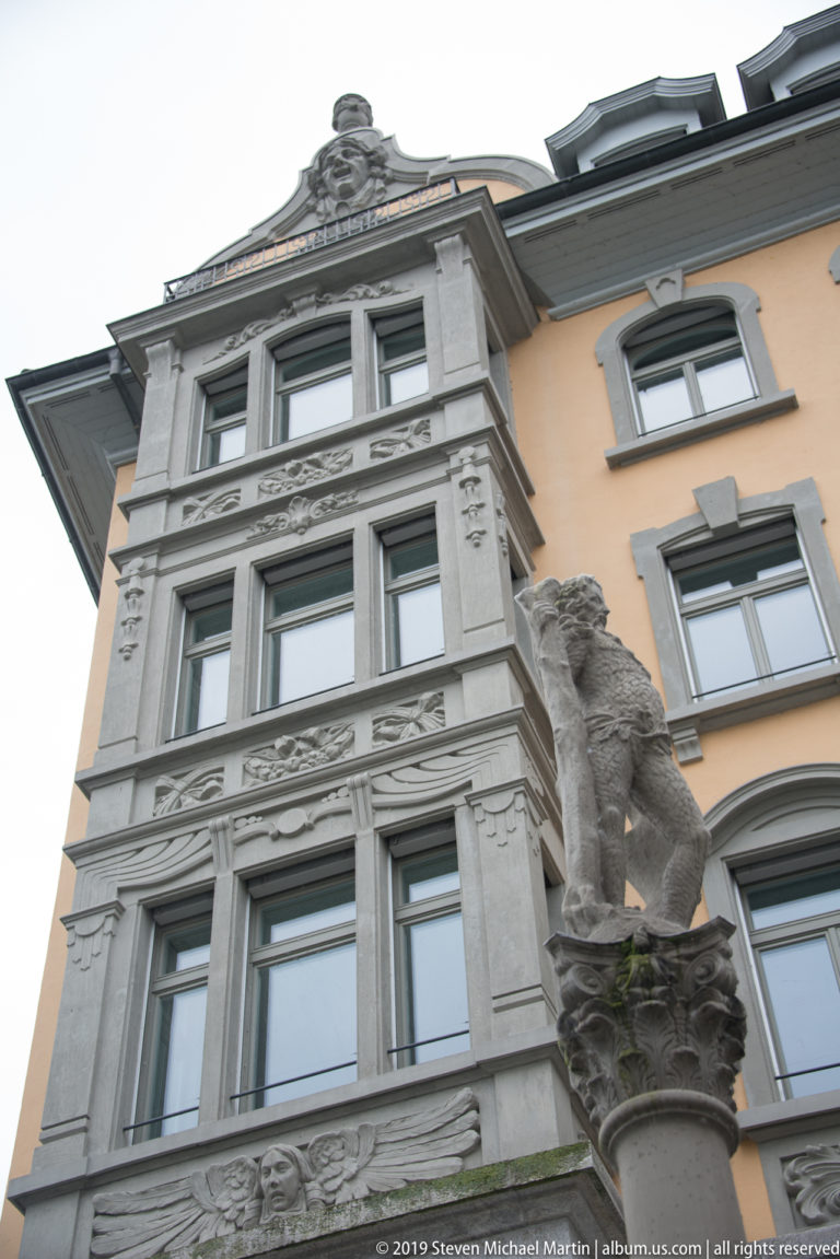 Upward view of an ornate historic façade with a sculpted lion projecting from the building corner.