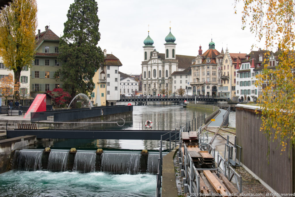 Reuss flowing over Lucerne’s needle dam with the twin-towered Jesuit Church and historic riverfront beyond.