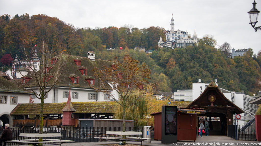 Autumn hillside above Lucerne with a prominent white historic building and tower rising over riverside structures.