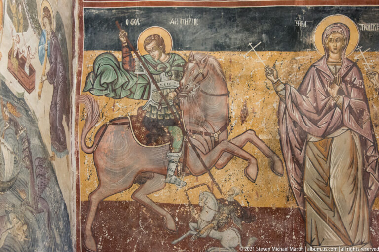 Mounted haloed warrior saint on horseback spearing a fallen figure, with a standing haloed woman at right.