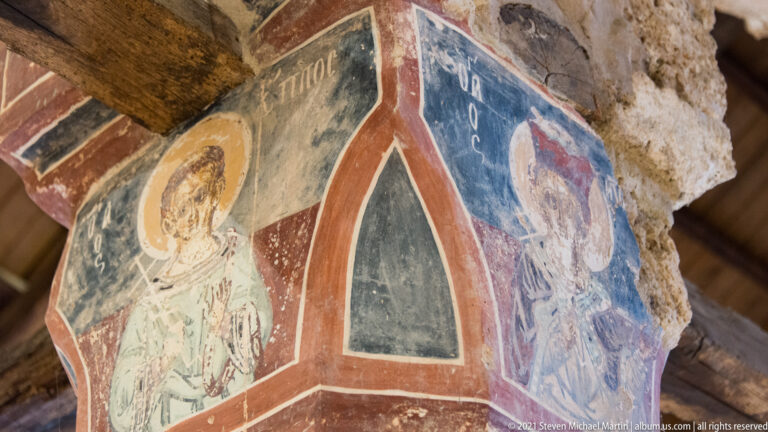 Oblique view of a masonry pier painted with haloed saints on adjacent faces and bordered in red.