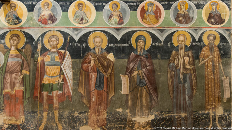 Row of full-length haloed saints beneath circular bust medallions on a dark fresco background.