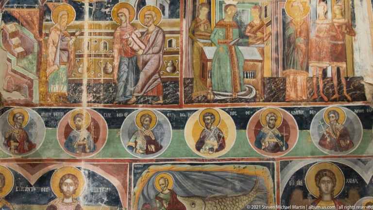 Wall fresco with upper narrative scenes, a row of saint medallions, and a lower Jonah-and-sea-creature panel.