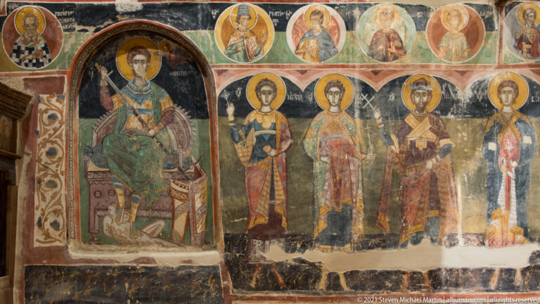 Enthroned haloed military saint in an arched panel beside a row of standing young haloed saints.
