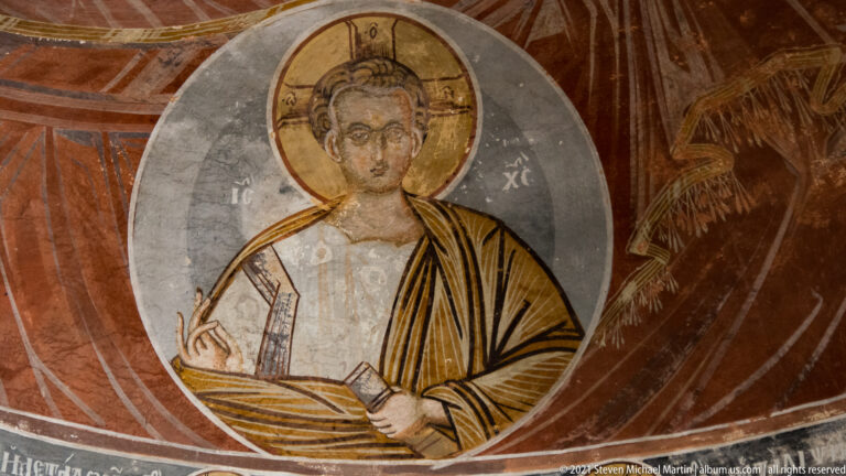 Half-length haloed Christ holding an open book against a dark painted background.