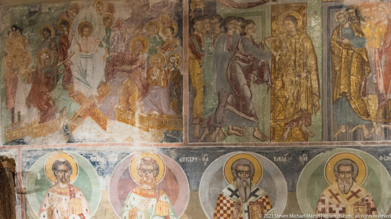 Weathered multi-register mural with narrative scenes above rows of haloed bishops and saints.