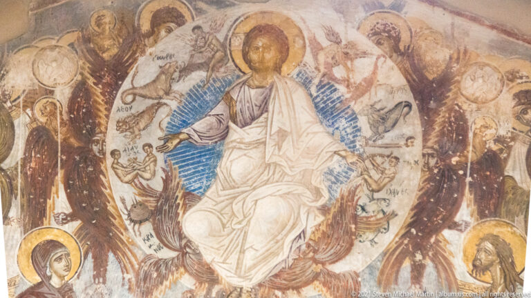 Christ seated frontally in a blue radiant mandorla, surrounded by winged heavenly forms and smaller haloed figures.