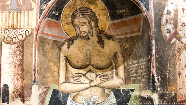 Close view of haloed Christ with bowed head, bare torso, and crossed arms against a dark niche.