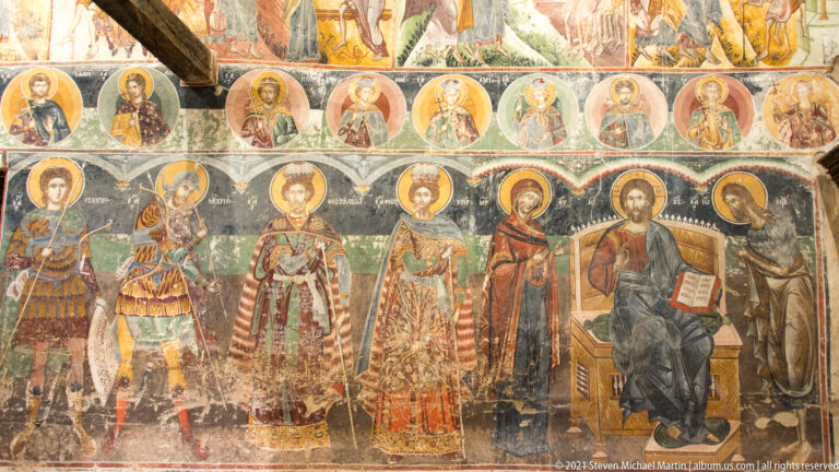 Row of haloed standing saints and an enthroned Christ holding an open book beneath smaller medallion figures.