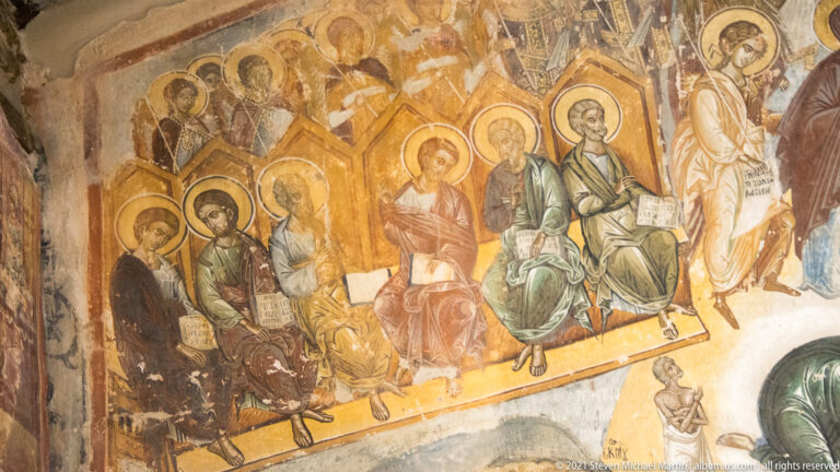 Row of seated haloed saints in colored robes, some holding books, against a warm ochre fresco ground.