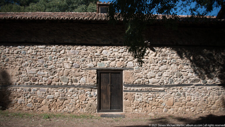 Close exterior view of irregular fieldstone masonry, a wooden door, and the projecting tiled roof.