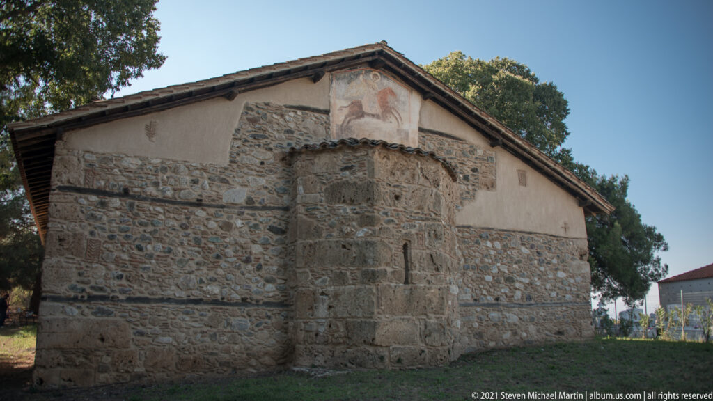 Exterior east end with a projecting polygonal stone apse, small slit openings, and gabled tiled roof.