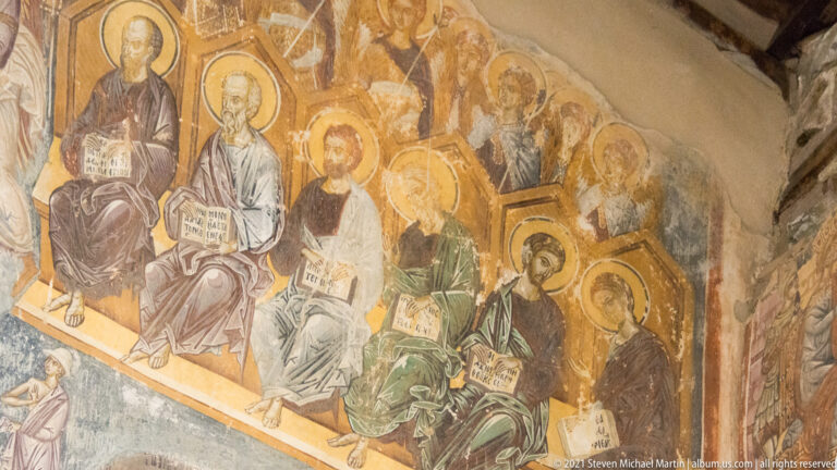 Seated haloed saints holding books in a fresco register that wraps around an interior wall corner.