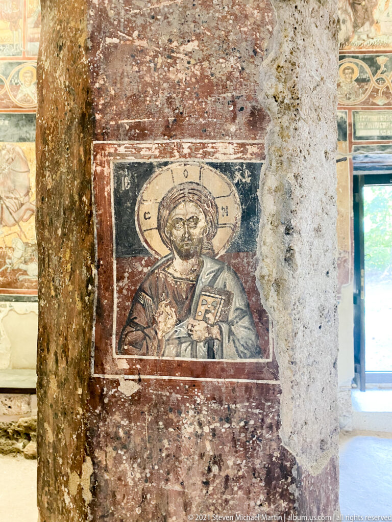 Half-length Christ with cross halo, raised blessing hand, and Gospel book painted on a masonry pier.