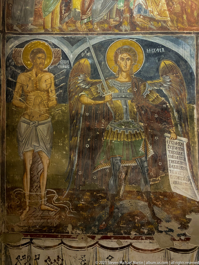 Armored Archangel Michael with wings and sword beside a wounded haloed youthful martyr.