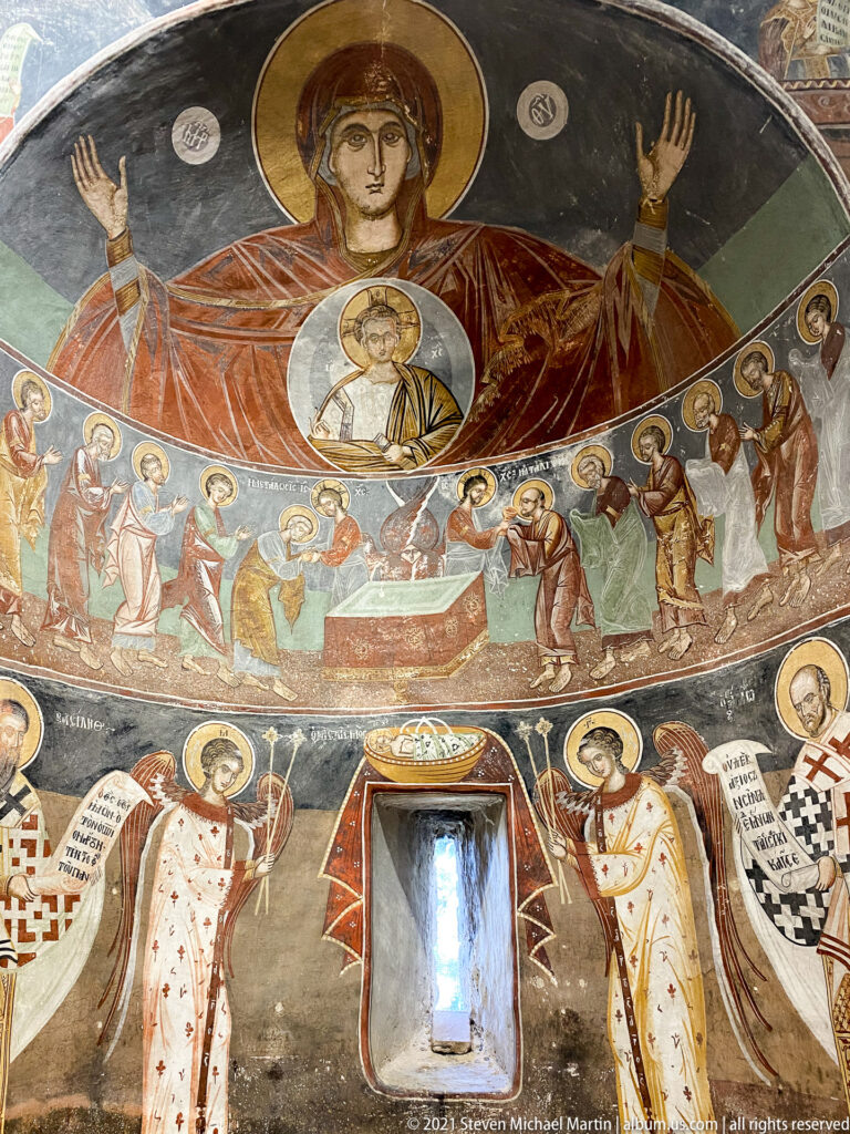 Apse fresco with Virgin Orans and Christ medallion above Communion scene and standing bishops around a window.