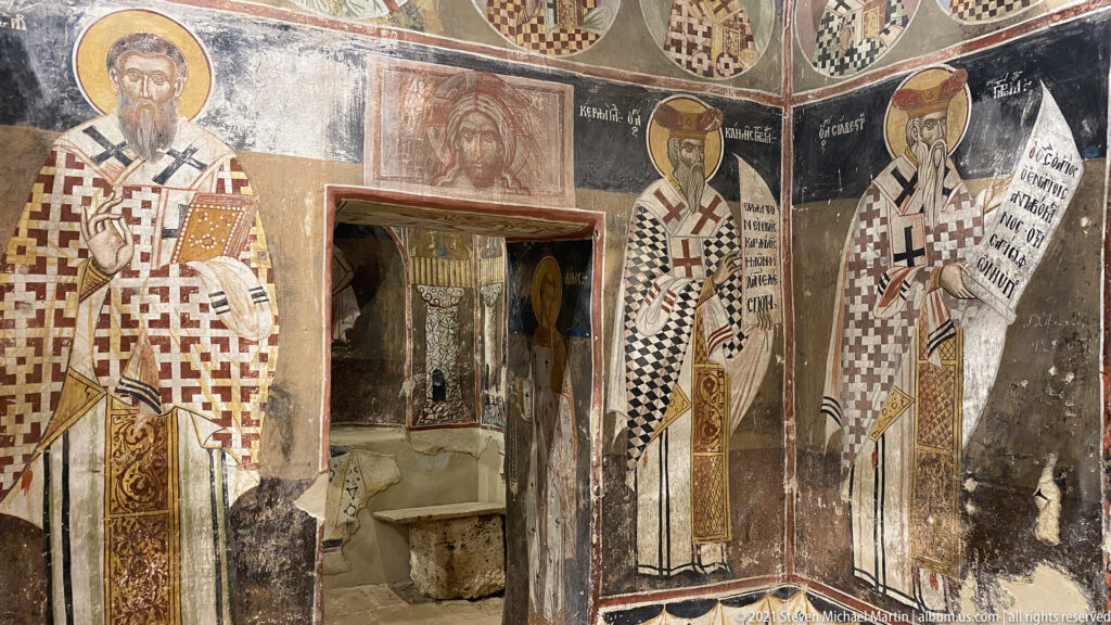 Large haloed bishops holding scrolls flank a doorway beneath painted medallions and additional wall figures.