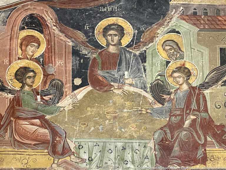 Three haloed angels seated at a table with Abraham and Sarah standing at the sides.