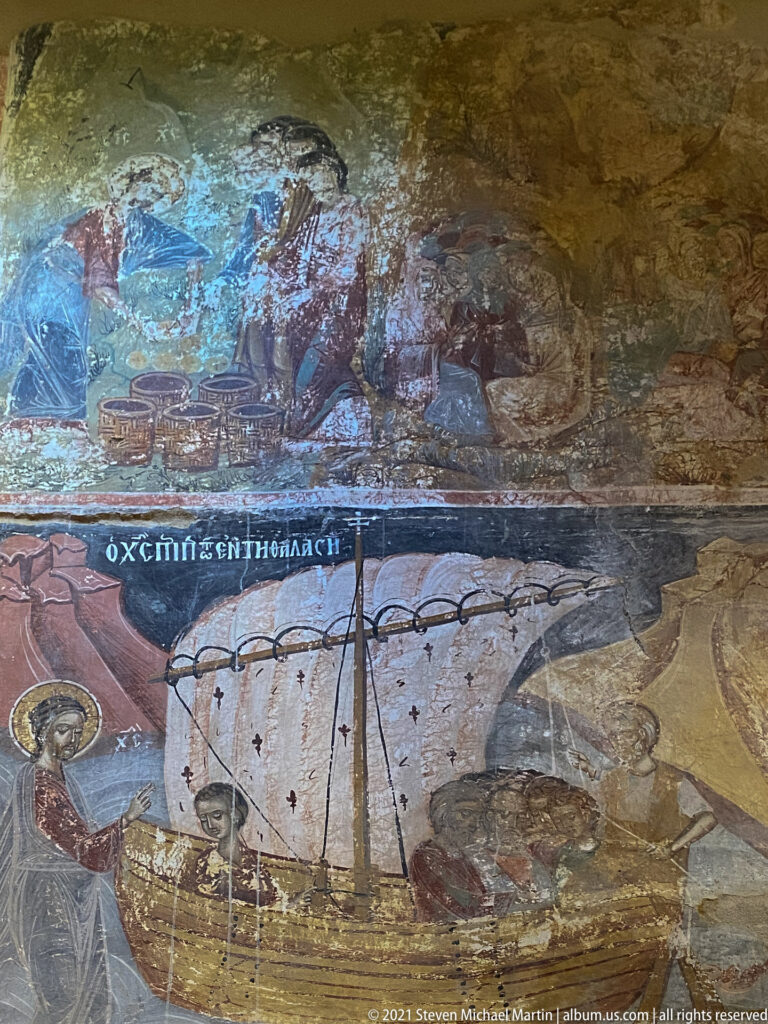 Fresco of a sailing ship with a large white sail and a figure cast toward the sea, with damaged scenes above.
