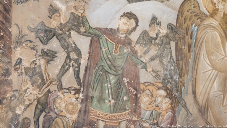 Central robed figure surrounded by dark demonic forms and clustered heads in a damaged fresco of punishment or torment.