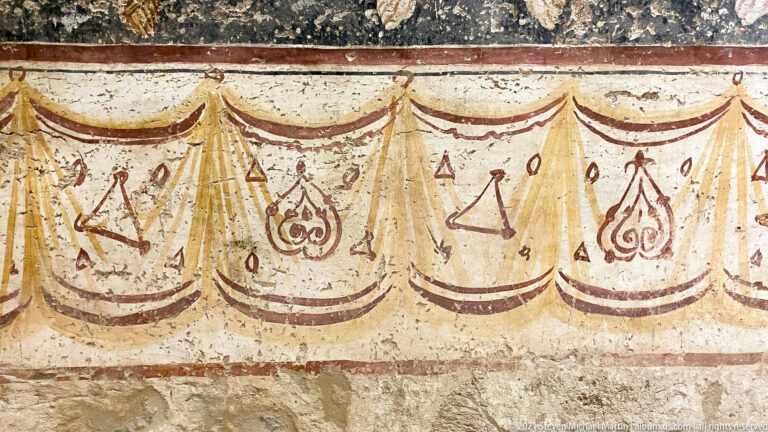 Painted curtain-like dado with scalloped swags and repeated red-brown geometric and vegetal emblems.