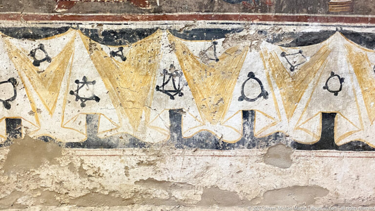 Yellow pointed curtain-like border with black symbolic motifs and areas of missing plaster along the lower edge.
