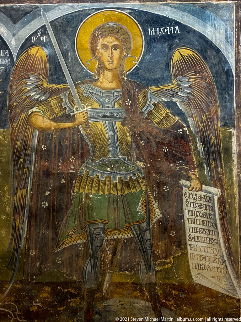 Armored winged Archangel Michael holding a sword across his chest and a long Greek-inscribed scroll.