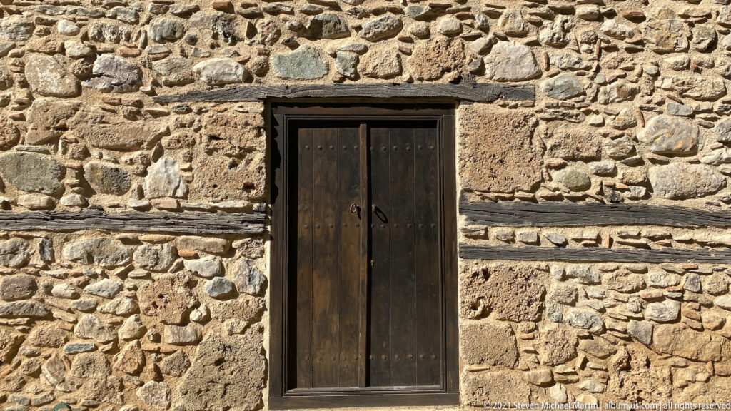 Dark wooden door set in an irregular stone-and-brick church wall with horizontal masonry bands.