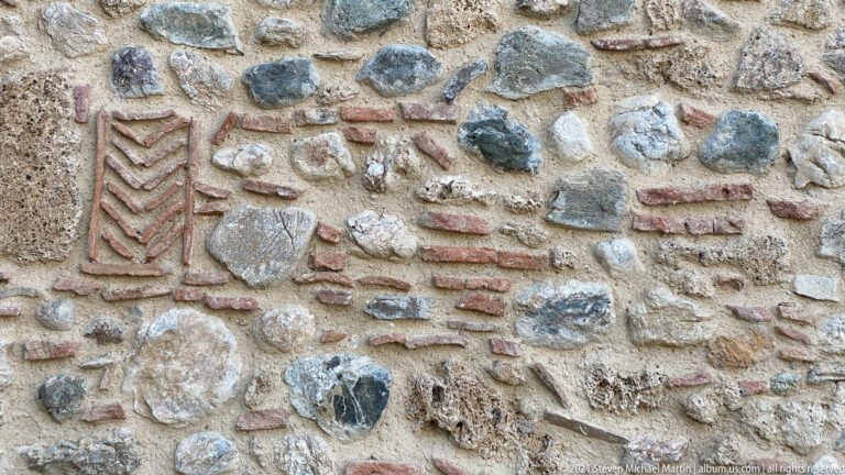 Rectangular herringbone brick panel and short brick courses embedded in irregular rubble-stone masonry.