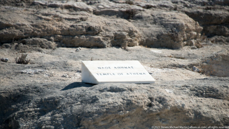 Bilingual stone marker reading “Temple of Athena” placed on weathered rock within the Ancient Kamiros archaeological site.