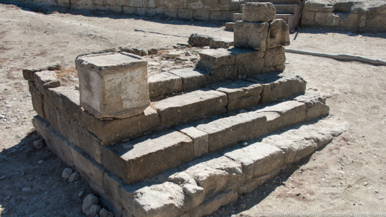 Three broad ancient stone steps leading to a low platform with fragmentary upright blocks at Ancient Kamiros.